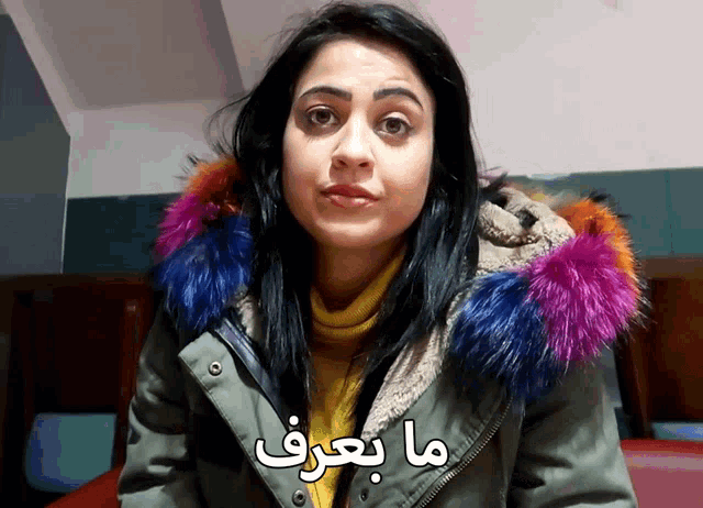 a woman wearing a green jacket with a multicolored fur hood says " ma beref "