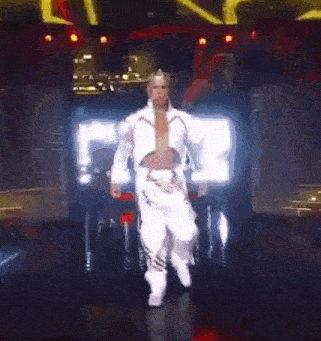 a man in a white outfit is walking on a stage with a microphone in his hand
