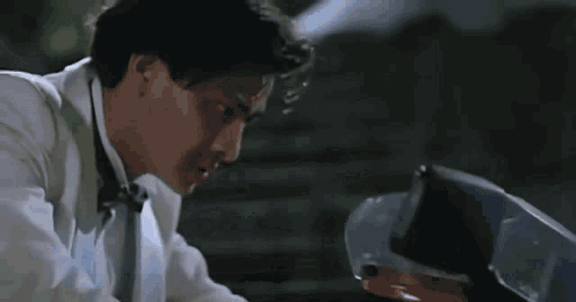 a man in a white shirt is sitting in a car with his head down .
