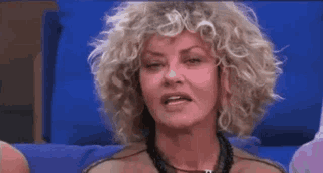 a woman with curly hair and a necklace is sitting on a blue couch with her eyes closed .