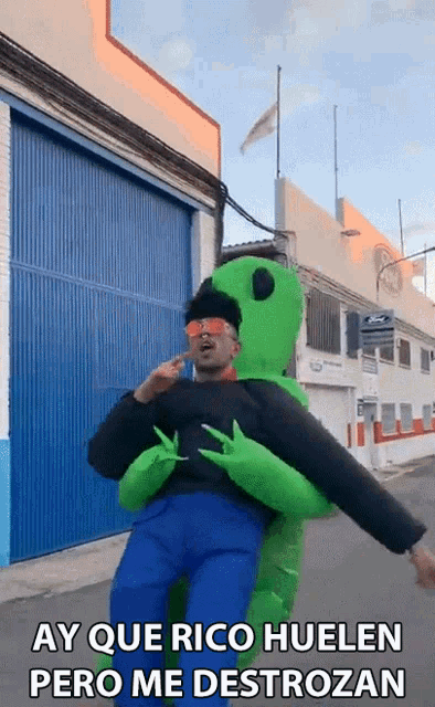 a man in a green alien costume is being held by another person