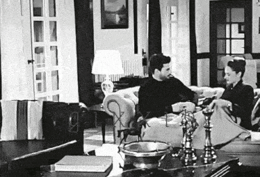 a black and white photo of a man and a woman sitting on a couch in a living room .