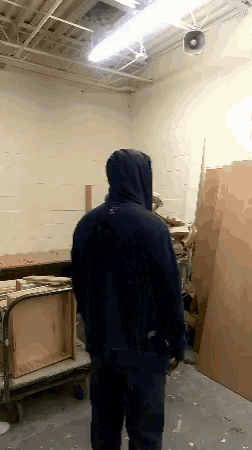 a man in a black hoodie is standing in a room with wooden boxes