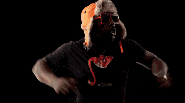 a man wearing an orange hat and sunglasses is dancing in the dark