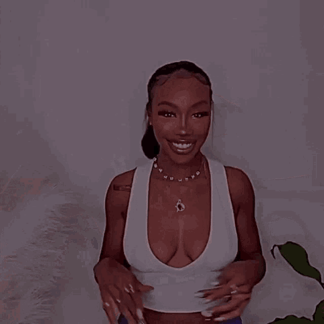 a woman wearing a white tank top and a necklace that says ' u ' on it