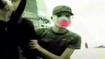 a man wearing a mask with a pink tape around his mouth is being held by another man
