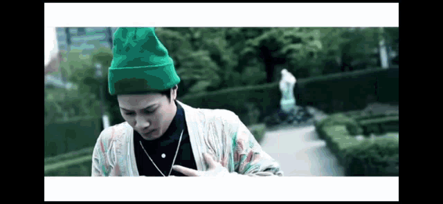 a man wearing a green hat and a necklace is standing in a garden .