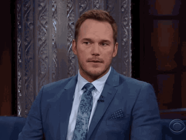 a man in a suit and tie is sitting on a cbs couch