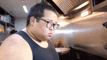 a man wearing glasses and a tank top is cooking in a kitchen
