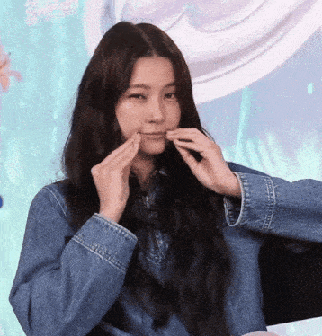 a woman wearing a denim jacket is touching her face