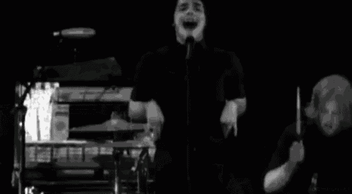 a black and white photo of a man singing into a microphone on stage .