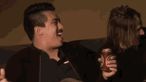 a man is sitting on a couch holding a can of soda and giving a middle finger .