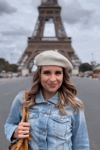 a woman wearing a white beret and a denim jacket stands in front of the eiffel tower .
