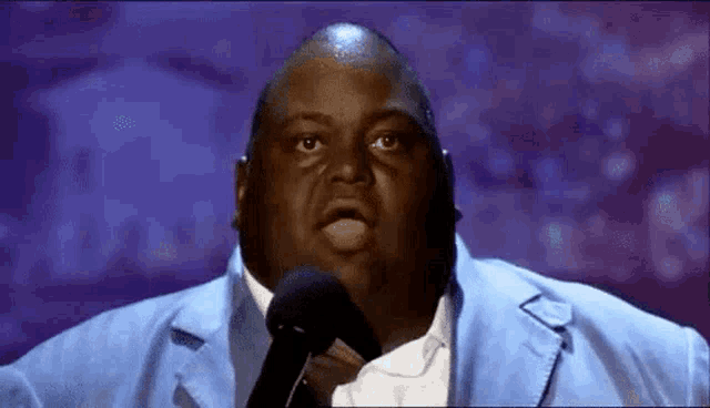 a man in a blue suit is holding a microphone and making a funny face .