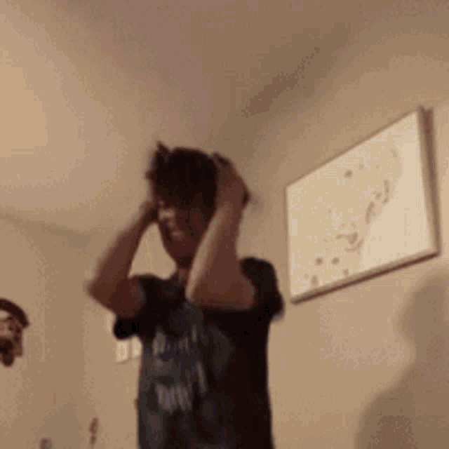 a man is standing in a room with his hands on his head and a picture on the wall behind him .