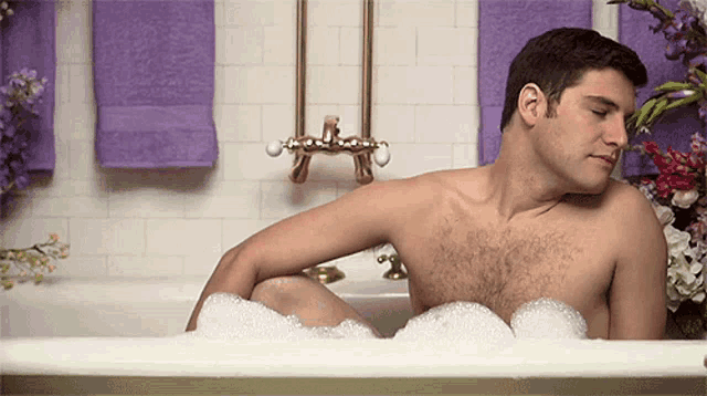 a shirtless man is sitting in a bathtub filled with foam