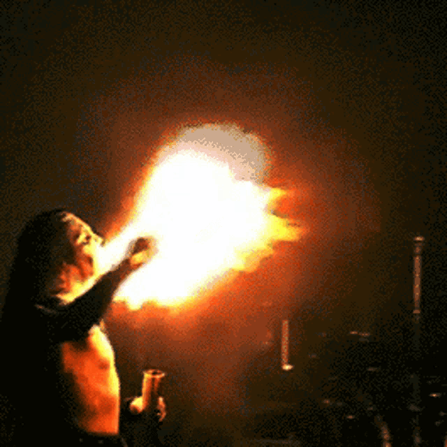 a man without a shirt is blowing fire in the dark