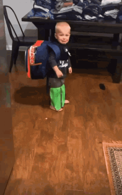 a little boy standing on a wooden floor with a backpack on his back that says bears on it