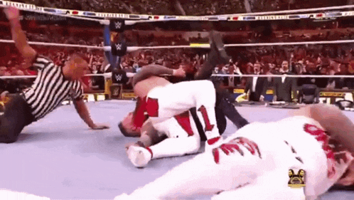 a wrestler is laying on the ground in a wrestling ring while a referee watches .