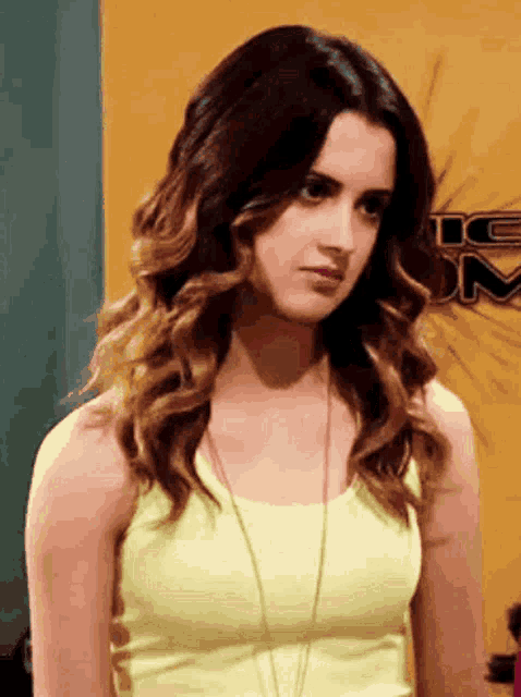 a woman wearing a yellow tank top stands in front of a sign that says ic on it