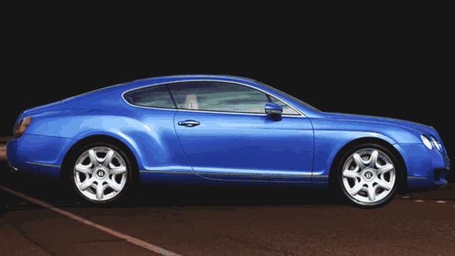 a blue bentley is parked on a dark road