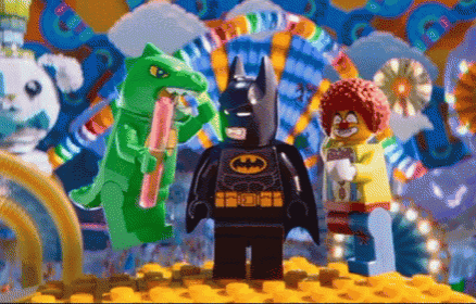 a lego batman stands in front of a clown and a green dinosaur