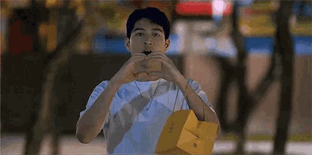 a young man is making a heart shape with his hands while holding a bag .