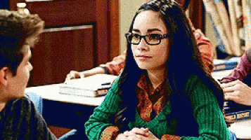 a girl wearing glasses and a green sweater is sitting at a desk with a boy .