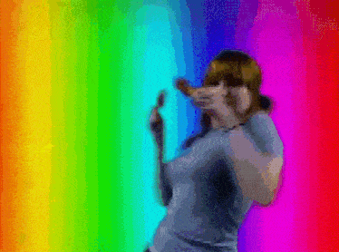 a woman is dancing in front of a rainbow colored background