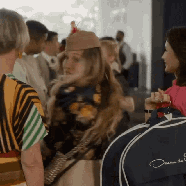 a woman wearing a hat is standing next to a woman wearing a oscar de la renta bag