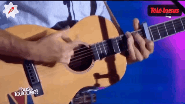 a man is playing an acoustic guitar with a tele loisirs logo in the background