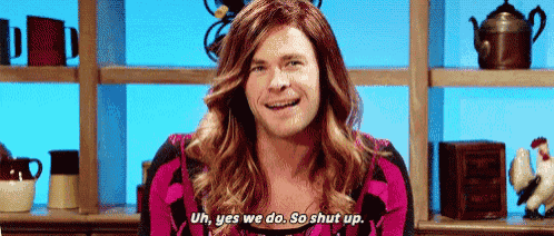 a man with long hair is sitting in front of a shelf .