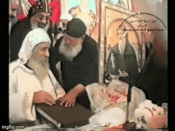 a man with a beard is holding a book in front of a microphone while other men look on .