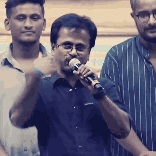a man with glasses is holding a microphone in front of another man