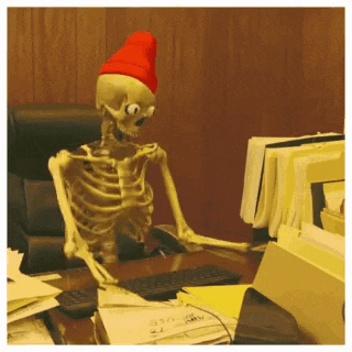 a skeleton wearing a red hat is sitting at a desk with a computer .