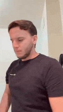 a man with a beard is standing in a room wearing a black t-shirt .