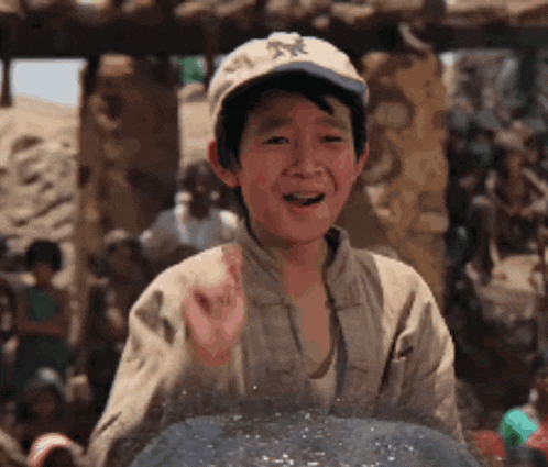a young boy wearing a hat is standing in front of a group of people and smiling .