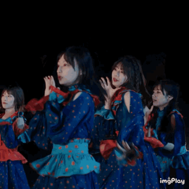 a group of girls in blue and red polka dot dresses are dancing in a dark room with the words imgplay visible in the corner