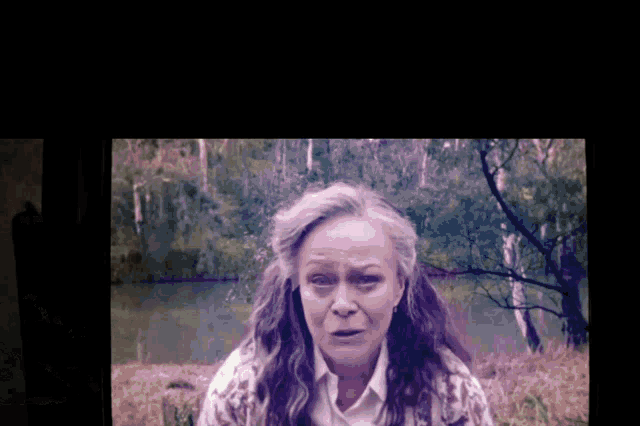 a woman with gray hair and a white shirt stands in front of a lake