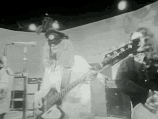 a black and white photo of a man playing a guitar in front of a microphone .