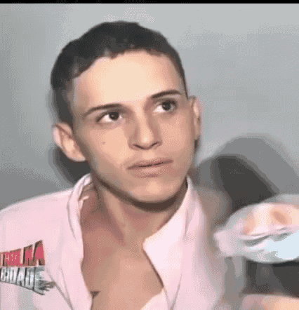 a young man wearing a pink shirt without a shirt is looking at the camera .