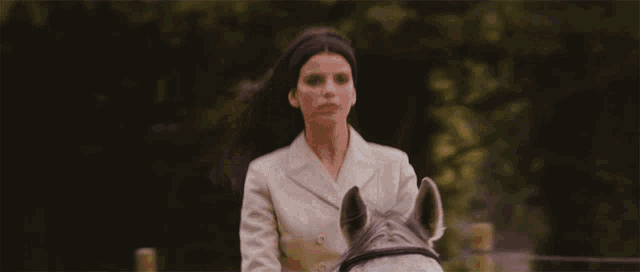 a woman in a white suit is riding a gray horse .
