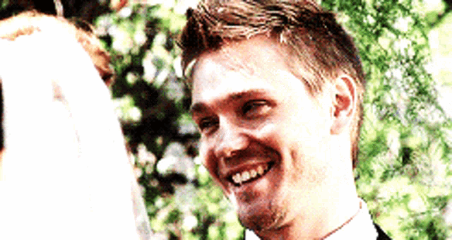 a man in a suit and tie is smiling while standing next to a woman in a white dress