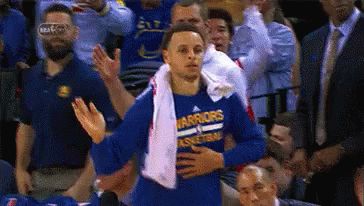 a basketball player wearing a blue shirt that says warriors on it is standing in front of a crowd .