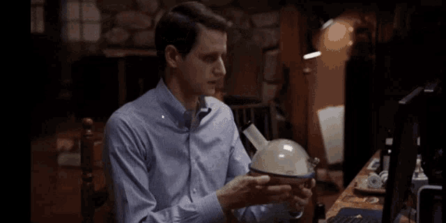 a man in a blue shirt is sitting at a table holding a globe in his hands .
