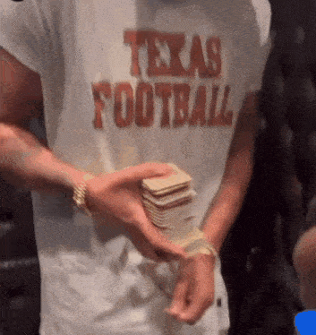 a man wearing a shirt that says texas football is holding a stack of money