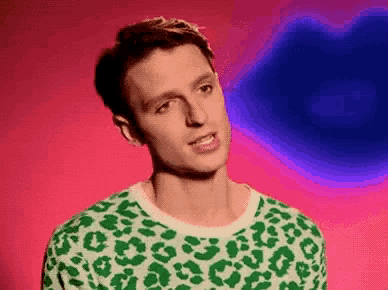 a man wearing a green and white sweater with a leopard print is standing in front of a pink background .