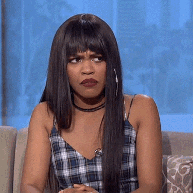 a woman with long hair is sitting on a couch and making a funny face .