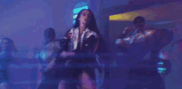 a woman in a black dress is dancing in a dark room with a neon sign in the background .