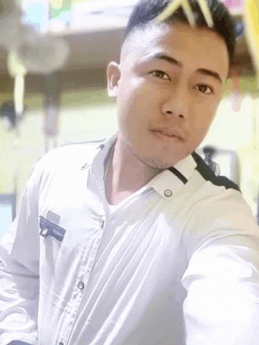 a man wearing a white shirt is taking a selfie with a pencil in his hair .